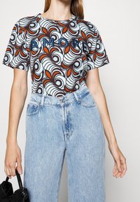 T-shirt with a swirling pattern in blue, brown, and orange, featuring the word "AMORE" in blue stitching. Paired with light-wash denim jeans.