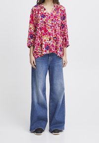 Blommig blus i rosa, blått och gult med långa ärmar, V-ringning och lös passform, matchad med vida blå denimjeans.