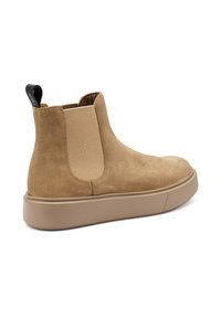 Botas Chelsea de ante en tono marrón claro, con paneles laterales de elastano y una lengüeta. Cuentan con una suela gruesa de goma beige para mayor comodidad y soporte.