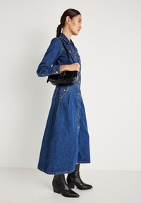 Blå denimkjole med lange ermer, knappelukking foran og en utsvingt skjørt. Kombinert med svarte høye støvler og en liten svart crossover-bag.