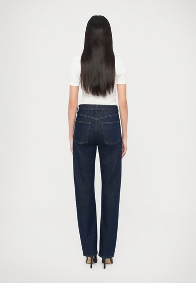 Tmavomodré rifle s vysokým pásom, rovnými nohavicami a zadnými vreckami. Kombinované s bielym priliehavým tričkom a lodičkami na ihličkovom opätku.