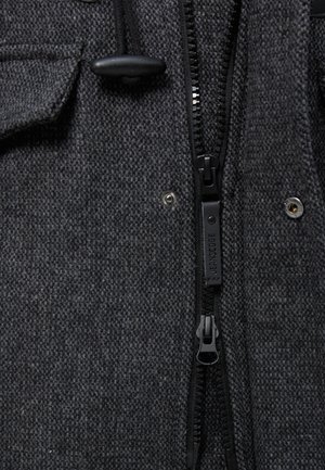 Gråt tekstureret jakke stof med en sort lynlås og to trykknapper. Elastisk snøre med plastikjustering ved kraven.