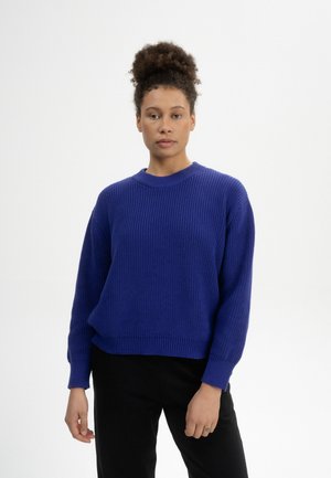 Strickpullover in leuchtendem Blau, mit Rundhalsausschnitt, gerippter Textur, überschnittenen Schultern und lockerer Passform, kombiniert mit schwarzen Hosen.