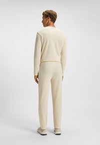 Ensemble de détente texturé de couleur crème, composé de manches longues et de pantalons. Design simple, avec des poignets et une taille ajustés. Des chaussures décontractées complètent le look.