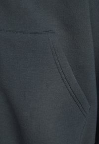 Hoodie gris foncé avec une poche avant, fabriqué en tissu doux avec une texture lisse et des coutures nettes le long des coutures.
