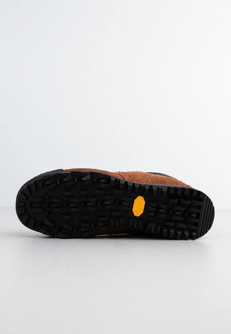 Semelle de chaussure en daim marron avec un fond en caoutchouc noir texturé, featuring un logo jaune et un motif de semelle rugueuse pour une meilleure traction.