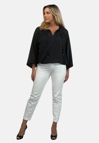 Czarna bluzka w groszki z dekoltem w literę V i luźnymi rękawami, zestawiona z białymi dopasowanymi spodniami i czarnymi szpilkami.