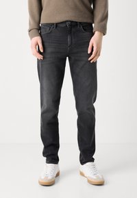 Black denim jeans with a slim fit, featuring five pockets, subtle whiskering on the thighs, paired with white sneakers.