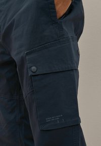 Mörkblå, lätta shorts i tyg med en sidoficka med knappstängning och tryckt textdetalj vid fållen.