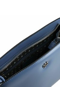 Blauwe leren handtas met een ritssluiting aan de bovenkant, voorzien van een zwart patroon aan de binnenkant en zilverkleurige accenten. Zeskantig logo als detail aan de buitenkant.