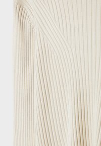 Gros plan sur un tissu en maille côtelée de couleur crème avec des lignes diagonales et verticales créant un motif texturé et plié.