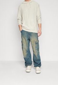 Ljust grått ribbat hoodie med känguruficka, ihopparat med urtvättade blå cargojens med sidofickor och en avslappnad passform. Vita sneakers.