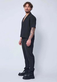 Chemise noire à manches courtes avec un design en V, associée à un pantalon noir et des bottes noires épaisses. Présente une coupe décontractée et une texture lisse.