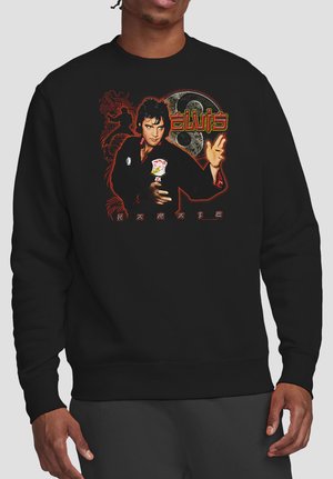 Mann trägt schwarzen Pullover mit Grafik von Elvis Presley in Karate-Pose, rotem Drachen, Yin-Yang-Symbol und dem Text "Elvis Karate."