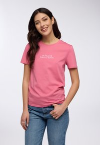 T-shirt di cotone rosa con maniche corte e collo rotondo, con testo bianco che recita "LA FELICITÀ PUNTO E BASTA."