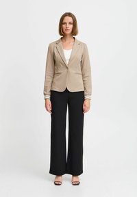 Hellbrauner Blazer mit einem einzigen Knopfverschluss, schmaler Schnitt und gestreiften Manschetten, kombiniert mit hoch-taillierten schwarzen weiten Hosen.