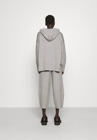 Szary bawełniany hoodie o luźnym kroju i dużym kapturze, zestawiony z dopasowanymi, luźnymi spodniami. Gładka tekstura, minimalny design, brak wzorów.