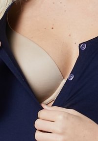 Beige bh delvis synlig under en marinblå skjorta med knappar i lila. Tyget ser slätt ut och framhäver bh:ns form.