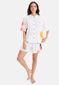 Kortærmet hvidt linnedskjorte og matchende shorts, der har orange blomster- og solmønstre, knaplukning fortil og afslappet pasform.