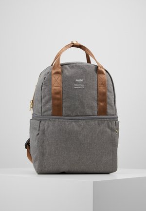 Mochila de tela gris con asas marrones, bolsillo delantero con cremallera y pequeño texto de marca blanco "anello" en la sección superior central.