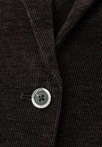 Ruskea corduroy-takki, jossa on teksturoitua kangasta, notched-käänteet ja hopeanvärinen nappi mustalla nelireikäisellä designilla.