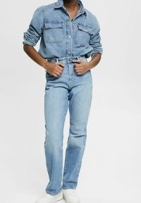 Ljusblå denimskjorta med två bröstfickor och knäppning, matchad med högmidjade ljusblå jeans och vita sneakers.