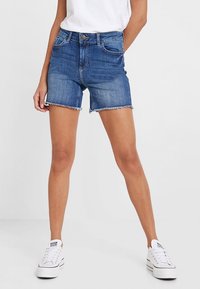 Jeansshorts i medelblått med fransig fåll, fem fickor och knappstängning framtill. Matchas med vita sneakers.