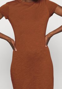 Ruskea neulemekko lyhyillä hihoilla, tiukka siluetti ja sileä pinta, jossa on hienovarainen heather-kuviointi koko matkalla.