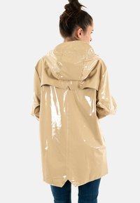 Impermeable beige brillante con capucha, de corte recto y parte trasera ligeramente más larga. Material texturizado y resistente al agua.