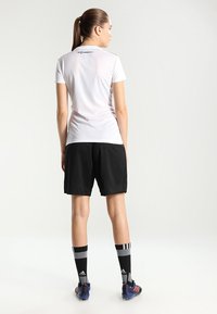 Witte sport t-shirt, zwarte shorts, zwart-grijze sokken en blauwe voetbalschoenen, met een logo op de achterkant van het shirt en strepen op de sokken.