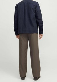 Tmavě modrá košile s dlouhým rukávem, rovného střihu a knoflíkovými manžetami, doplněná hnědými kalhotami s širokými nohavicemi. Látka má texturovaný vzhled.