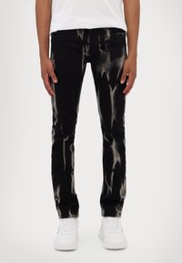 Svarta denimjeans med en slitna, blekta mönster; slim fit med fem fickor och dragkedja, kombinerat med vita sneakers.