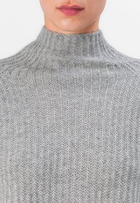 Grå stripet genser med høy hals. Laget av strukturert strikket stoff, med vertikale striper og en tettsittende design.