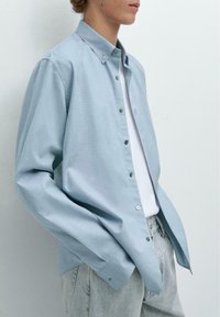 Himmelblaues Langarmhemd mit Button-down-Kragen, vorderen Knöpfen und einem lockeren Schnitt, kombiniert mit hellen Jeans.
