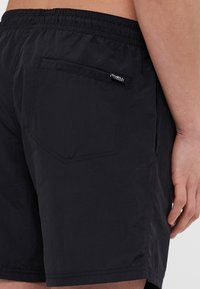 Pantaloni da nuoto neri con vita elasticizzata, tasca posteriore, etichetta logo discreta e una texture di tessuto liscia e leggera.