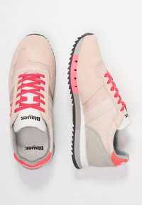 Zapatillas deportivas en rosa claro con materiales de ante y malla, un panel texturizado, cordones rosas y una suela de goma gris con detalles en rosa.