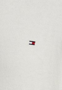 Suéter de malha bege claro com um pequeno logótipo bordado em vermelho, branco e azul na área do peito esquerdo.