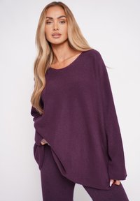 Lila oversized Pullover aus weichem Stoff, mit Rundhalsausschnitt, langen Ärmeln und lockerem Schnitt. Glatte Textur mit minimalen Details.