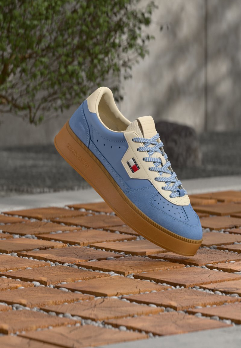 Baskets bleues et crème avec semelle en gomme et lacets à damier suspendues au-dessus de carreaux en bois et de petites pierres grises en plein air.