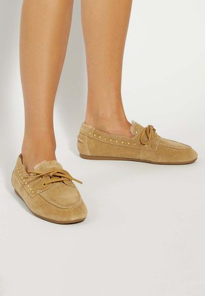 Tan suede loafers with a lace tie, gold studs along the upper edge, and a soft fluffy lining. Flat soles for comfort.