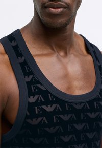 Top negru fără mâneci, cu un model repetitiv de logo, realizat dintr-un material moale, având un guler rotunjit și bretele late pentru confort.