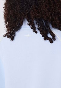 Sweatshirt bleu clair avec une texture douce, présentant un accent étoile blanche à l'arrière près de l'encolure et un design simple.