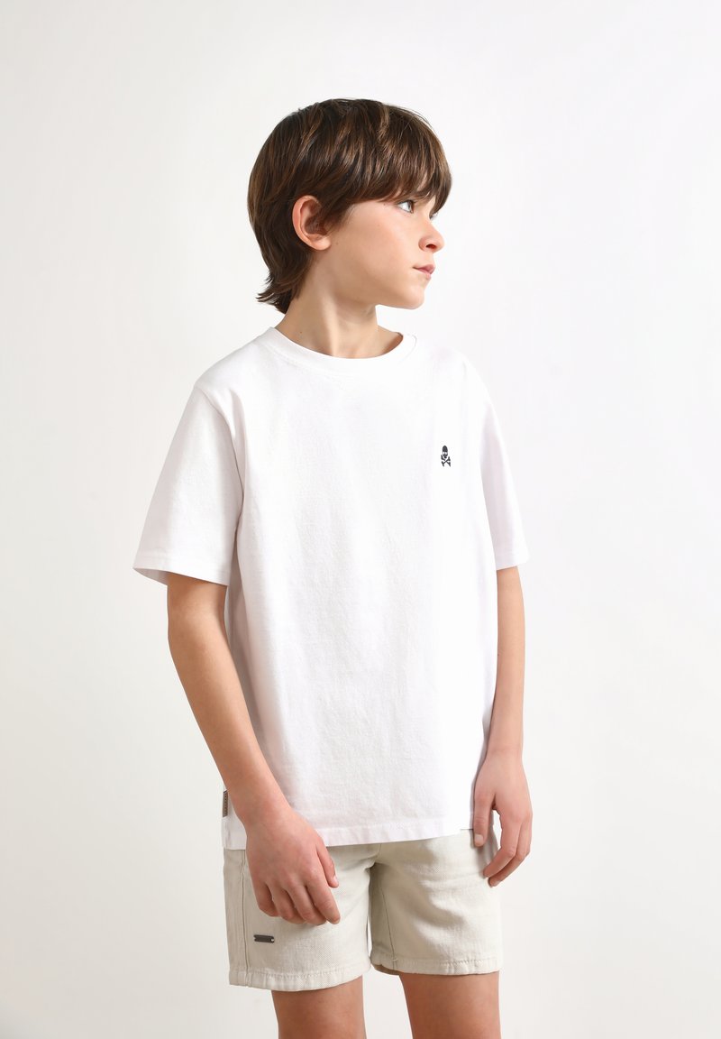 Witte katoenen T-shirt met korte mouwen, voorzien van een klein zwart logo op de borst. Gecombineerd met lichtbeige shorts met een subtiel detail.