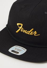 Svart caps med gult "Fender" broderi, som har en grønn tauak sjø på skjermen. Merket indikerer at visiret er laget av resirkulerte fiskegarn.
