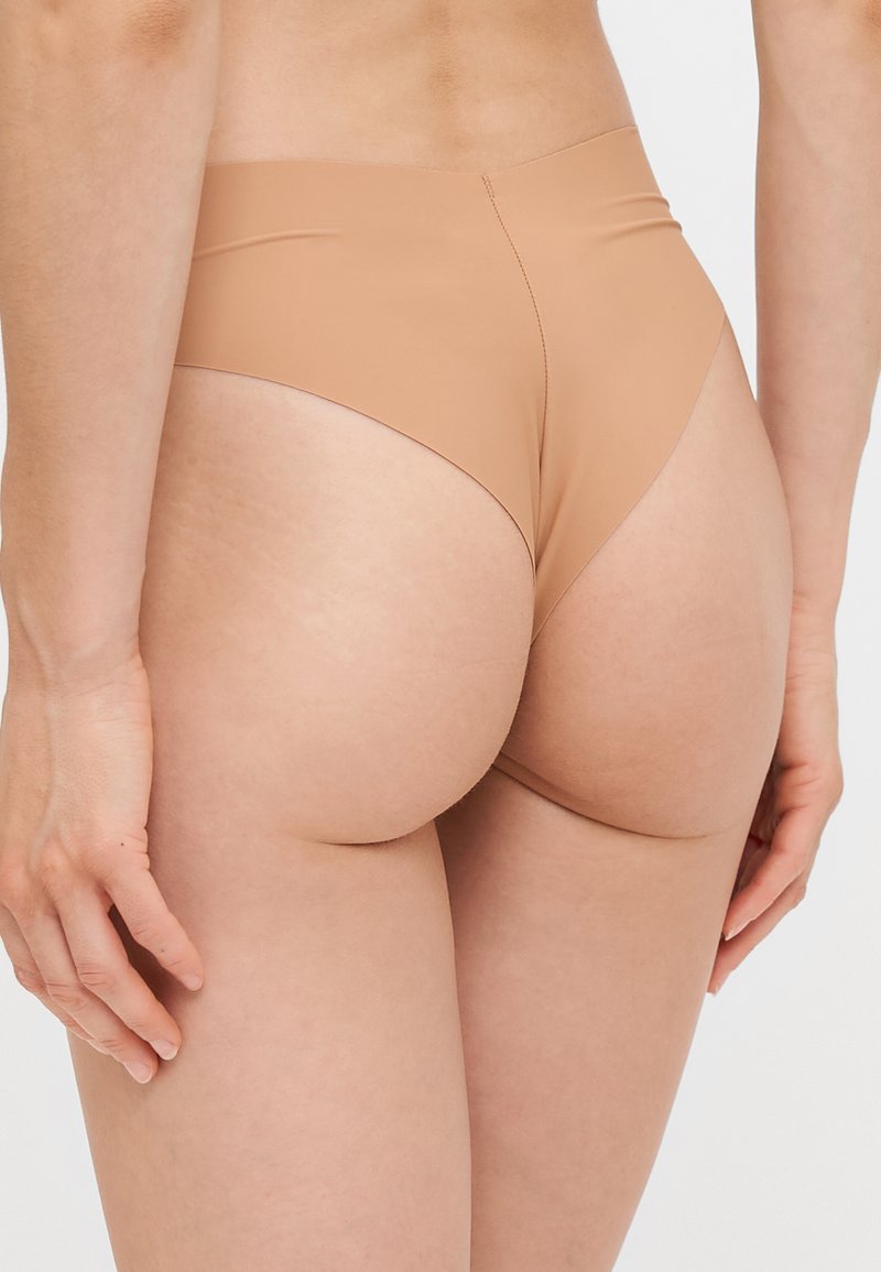 Hochgeschnittene Bikiniunterteile in Beige aus glattem, dehnbarem Material, das minimalen Schutz bietet und nahtloses Design aufweist.