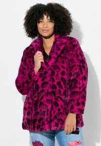 Abrigo de piel sintética en un vibrante color rosa con manchas de leopardo negras, con un cuello chal y un corte holgado, llevado sobre una camiseta negra y jeans de mezclilla.