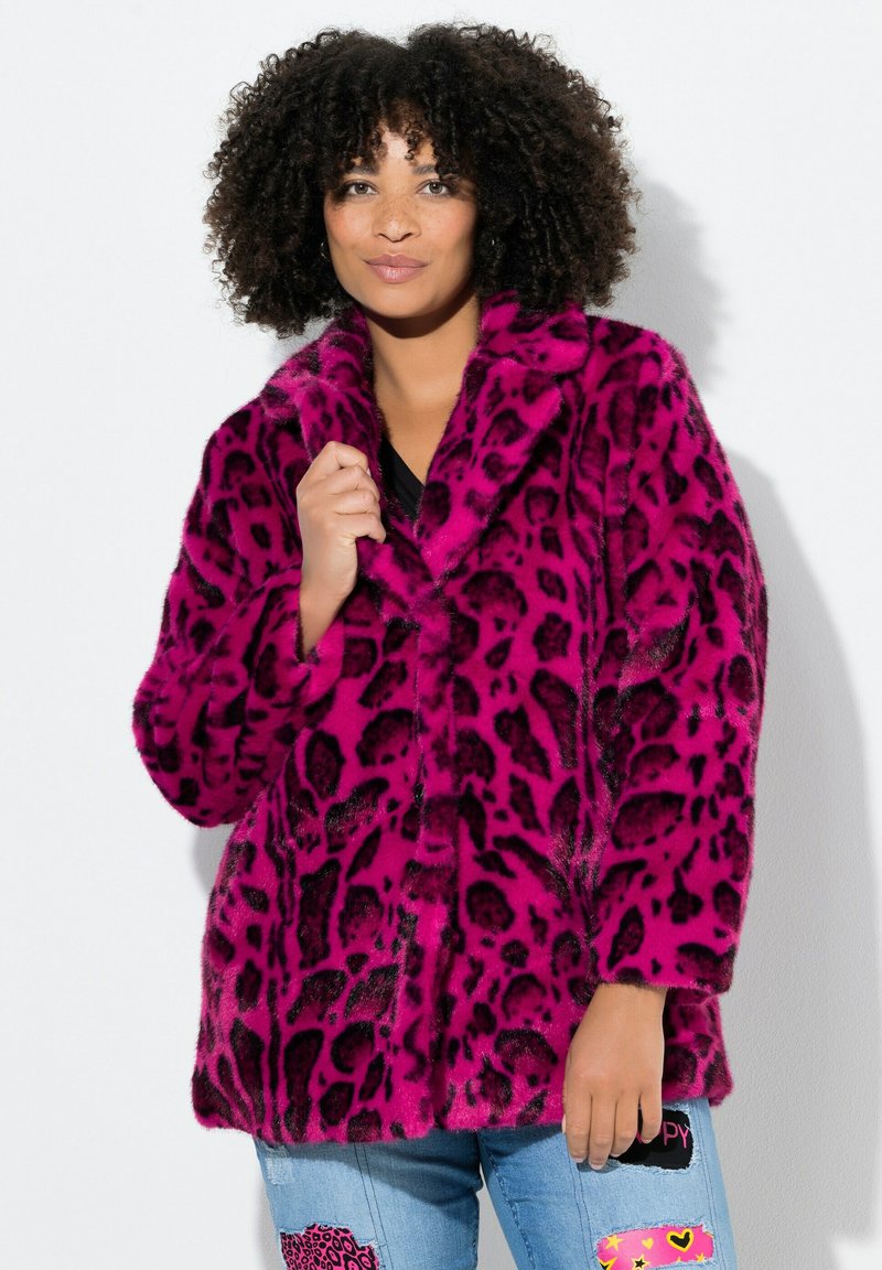 Abrigo de piel sintética en un vibrante color rosa con manchas de leopardo negras, con un cuello chal y un corte holgado, llevado sobre una camiseta negra y jeans de mezclilla.