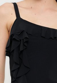 Μαύρο τοπ χωρίς μανίκια με λεπτές τιράντες και στρωτό βολάν κατά μήκος του ντεκολτέ και της πλευράς.