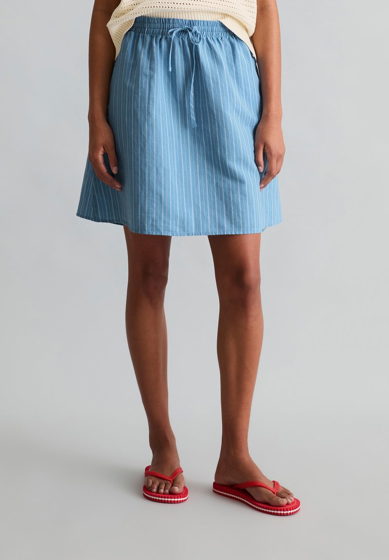 Woman wearing a blue striped knee-length skirt with a drawstring waist and red flip-flops, standing against a plain background.