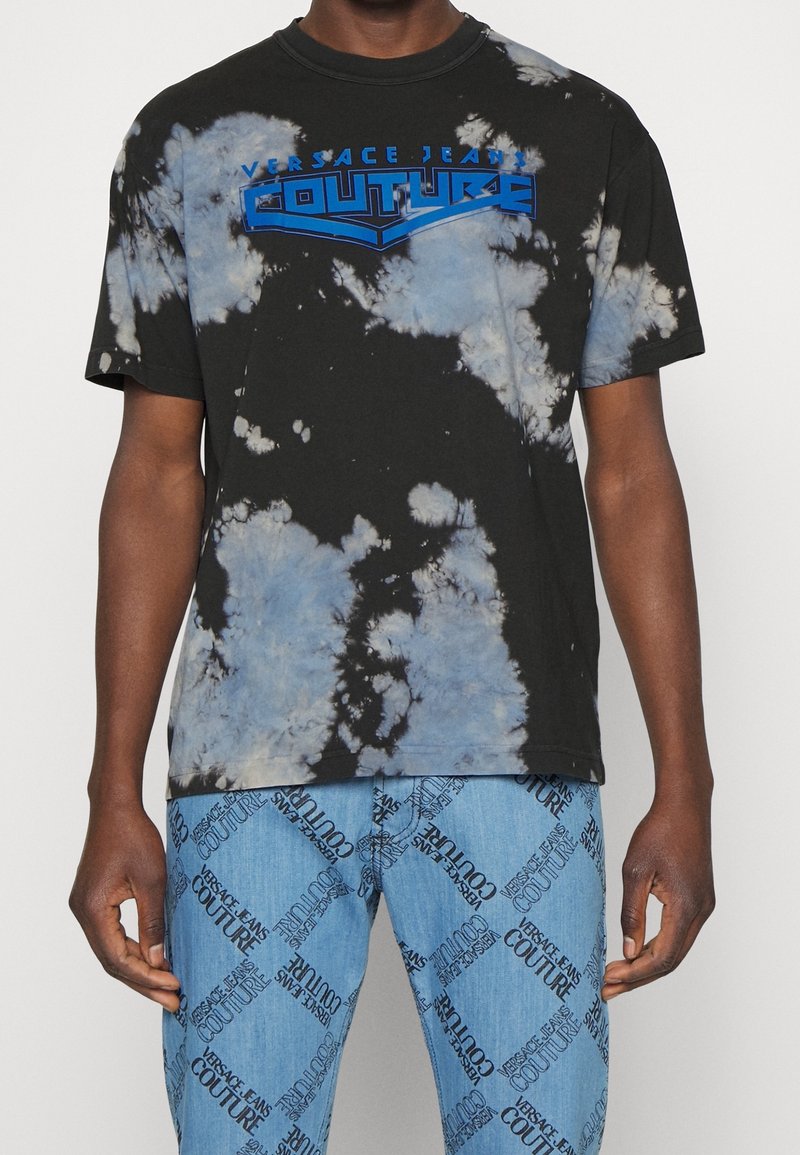 Schwarzes Batik-T-Shirt mit einem blauen "Versace Jeans Couture" Logo. Kurze Ärmel, runder Halsauschnitt und eine lockere Passform.
